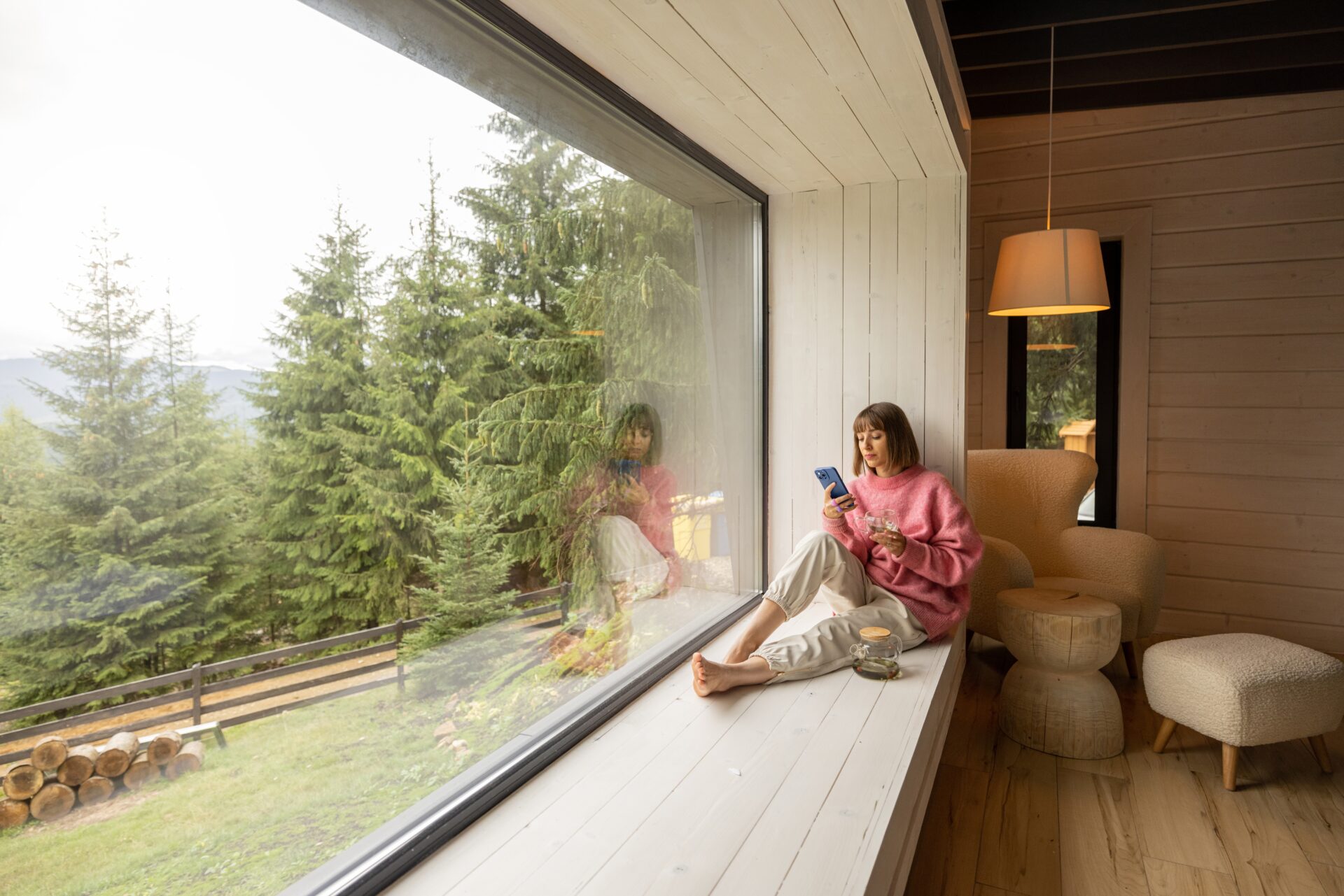 Woman,Sits,With,Phone,On,Window,Sill,And,Enjoys,Scenic